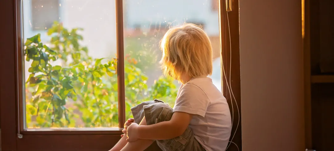 Niño pequeño mirando por la ventana dentro de su casa
